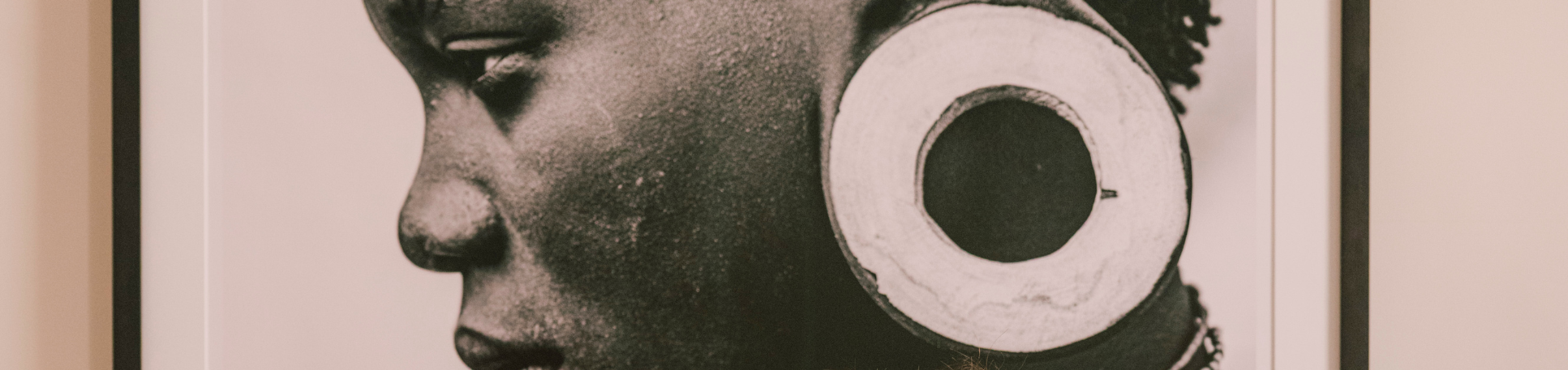 Black and white portrait of a person wearing large circular earrings with a beige border.