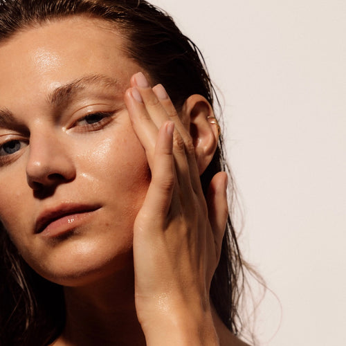 Close-up of a woman applying LAST Fundamental Serum to her face with a neutral background