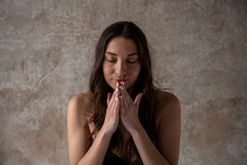 Woman with hands pressed together in front of her face against a textured brown wall, smelling LAST Skin Repair Serum