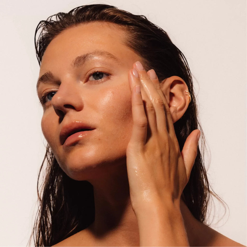 LAST skincare Woman with wet hair touching her face while applying a LAST Fundamental Serum against a plain background